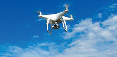 A photograph of a drone flying in the blue sky with clouds