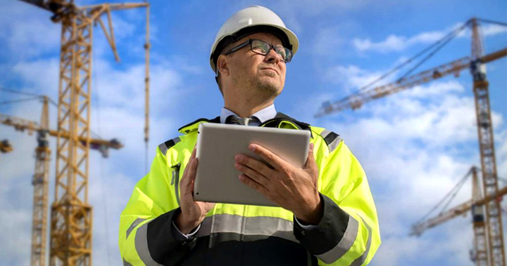 Inspector at an outdoor construction job site inspecting data on a tablet in PPE