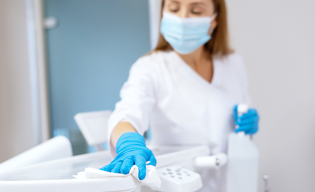 A photograph of a healthcare worker wearing a mask, scrubs, and gloves diligently disinfecting a surface.