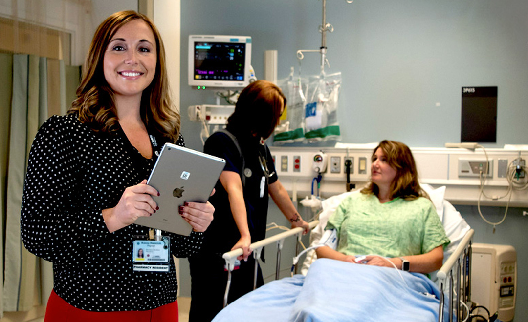 EHS specialist smiling with ipad as nurse checks in with patient in the background