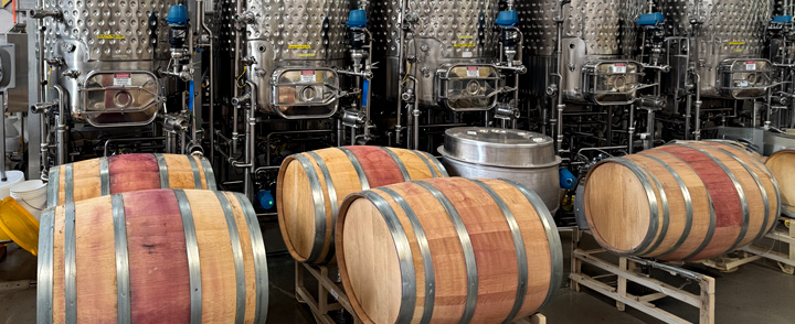 Wine barrels in front of stainless steel fermentation tanks in a winery.