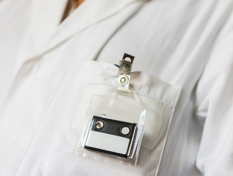 A close-up image of a white lab coat featuring a dosimetry badge attached to the chest area, used for monitoring radiation exposure levels in occupational settings