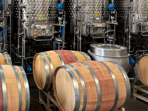 Wine barrels in front of stainless steel fermentation tanks in a winery.
